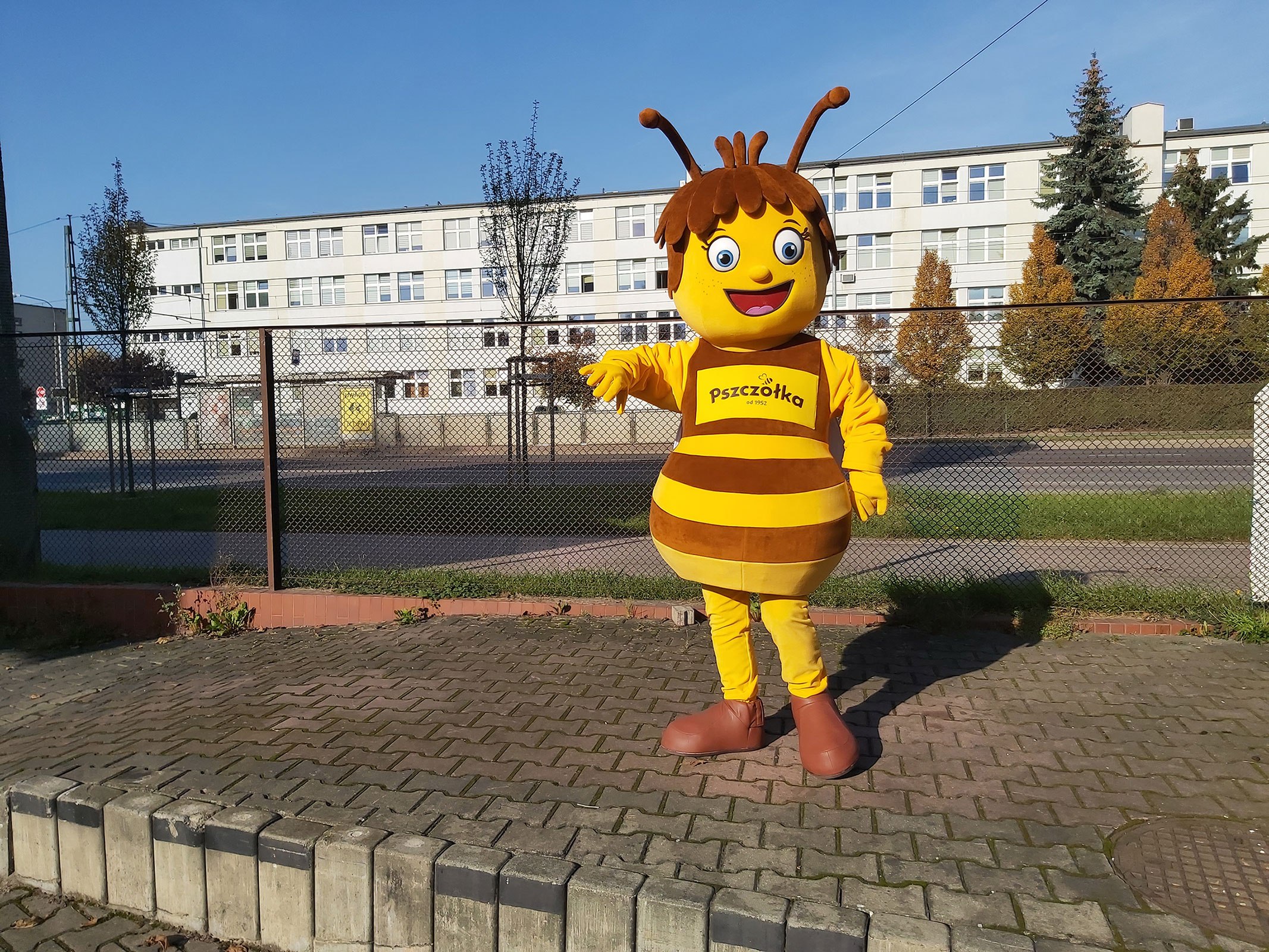 Na fotografii widnieje strój reklamowy w postaci pszczoły pozujący do fotografii przed siedzibą firmy Elabika